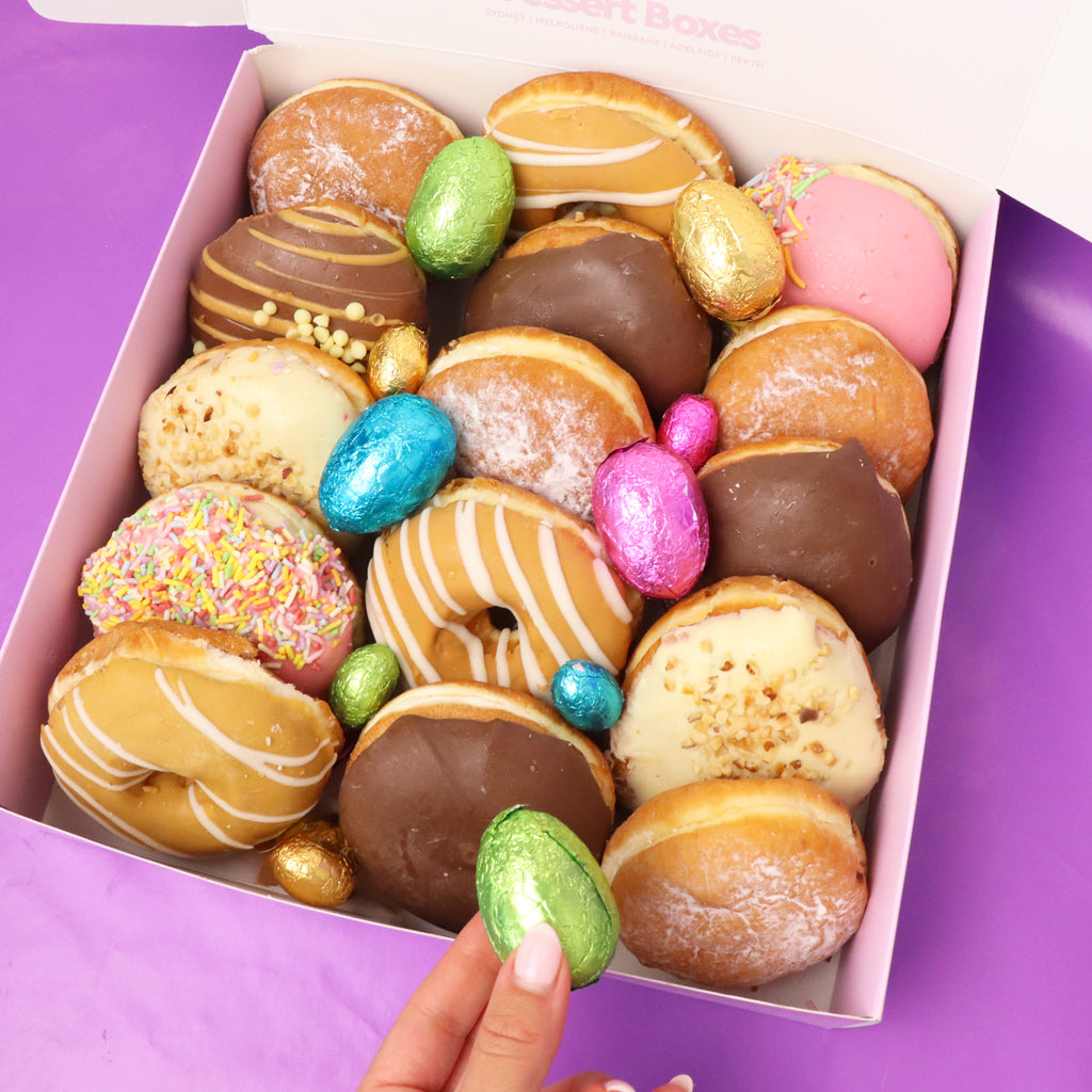 Box of assorted donuts with colorful Easter eggs on a purple background