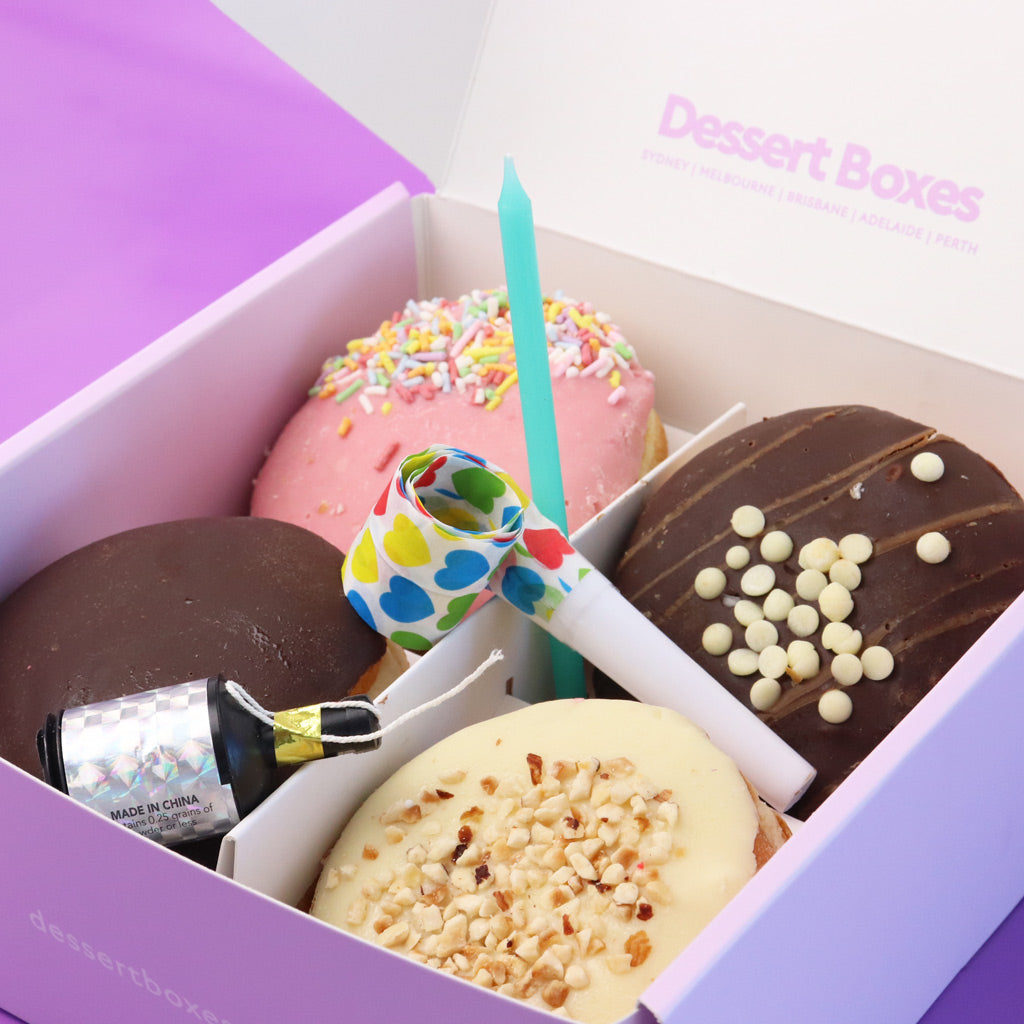 Assorted donuts in a dessert box with a candle and popper, branded 'Dessert Boxes'.