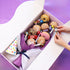 Box of donuts and snacks with a colorful towel on a purple background