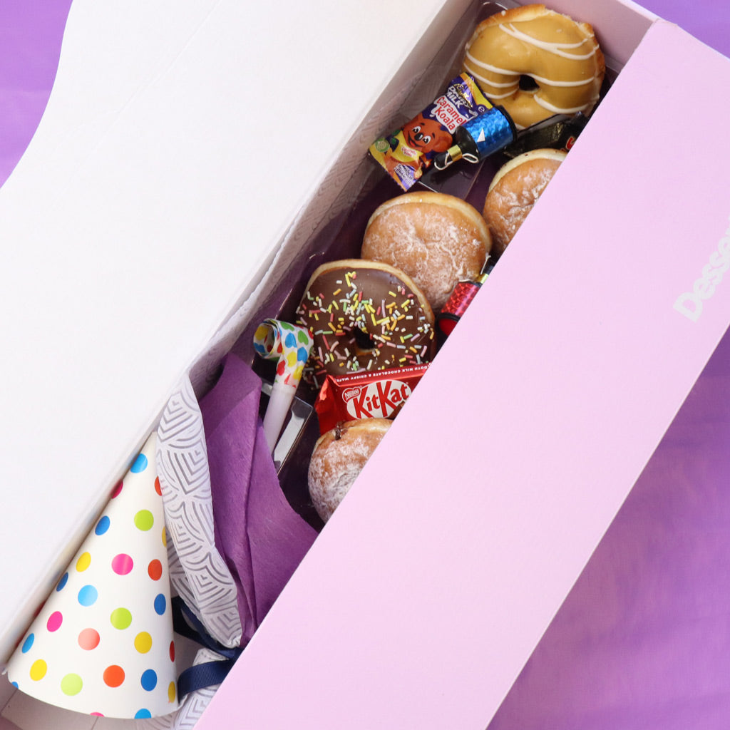 Assorted donuts and a colorful polka dot cone in a purple box.