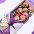 Box of assorted donuts, candies, and a bouquet with a colorful candle on a white background
