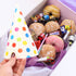 Colorful polka dot party hat held over a box of donuts and candy.