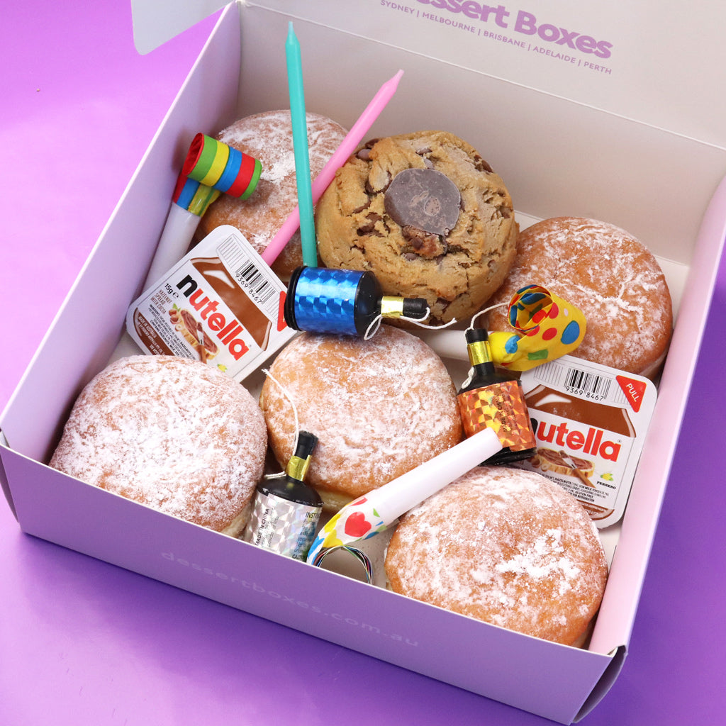 Box of Nutella donuts with Nutella packets and birthday popper on a purple background
