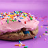 Cookie with pink frosting and colorful sprinkles on a purple background