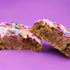 Sugar cookie with pink frosting and colourful sprinkles on a purple background