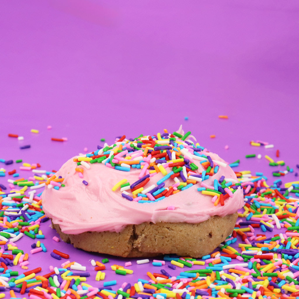 Cookie with pink frosting and colourful sprinkles on a purple background