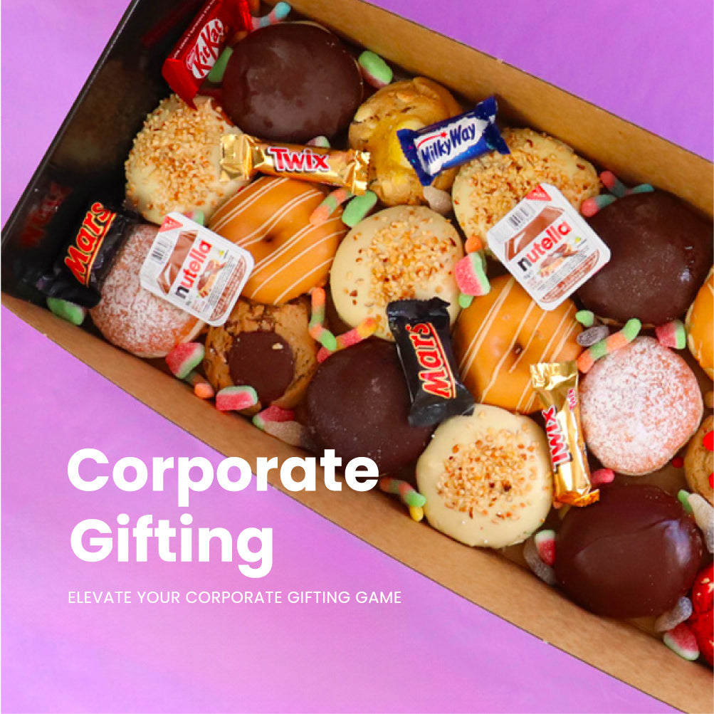 Assorted candies and cookies in a box with visible brand labels on a pink background, featuring text 'Corporate Gifting'.