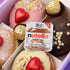 Box of assorted donuts with a Nutella spread container in the centre with Ferrero Rocher and Heart Chocolates.