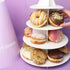 Three-tiered display of donuts and cookies with a hand reaching for a donut against a purple background.