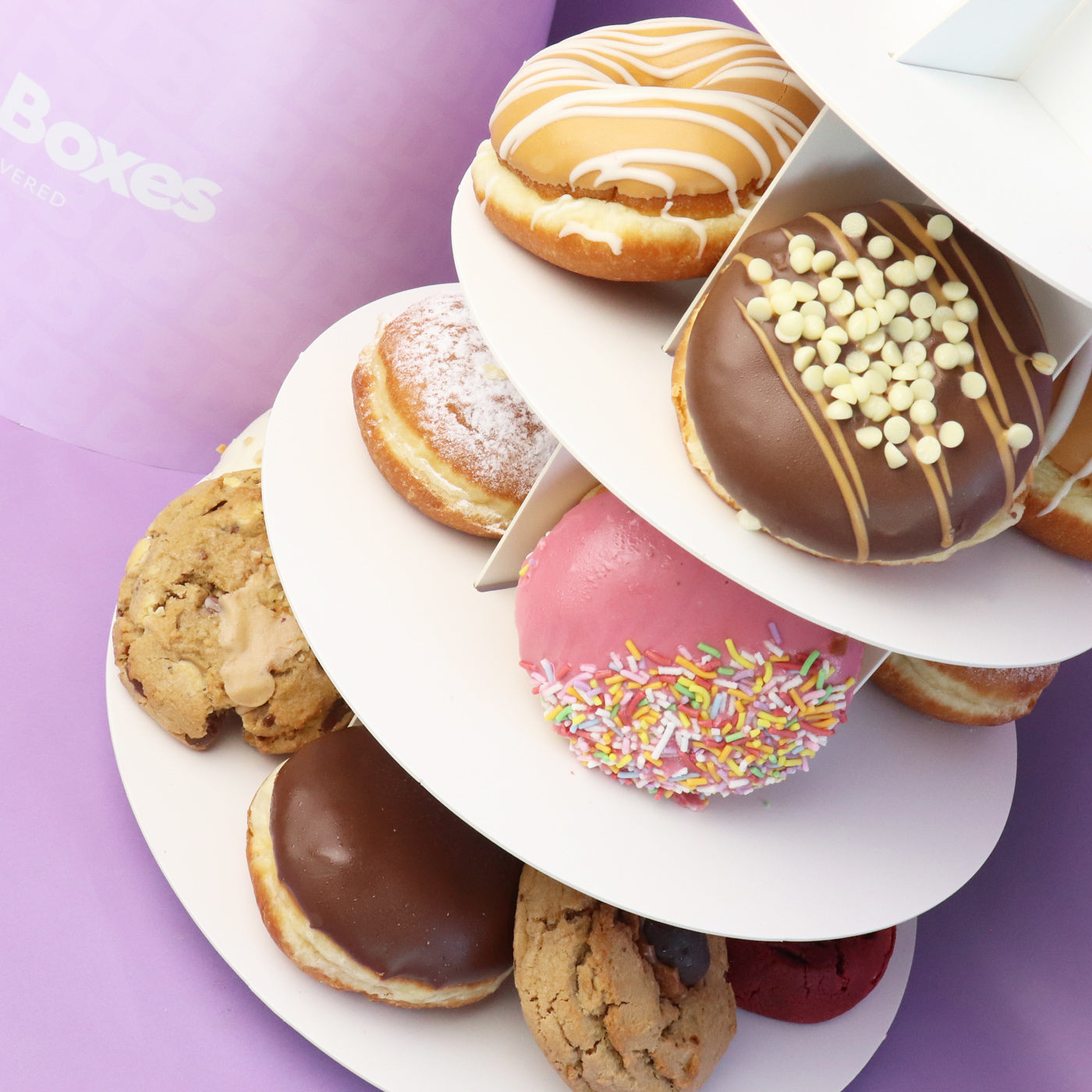 Assorted donuts and cookies on a tiered stand with a purple background