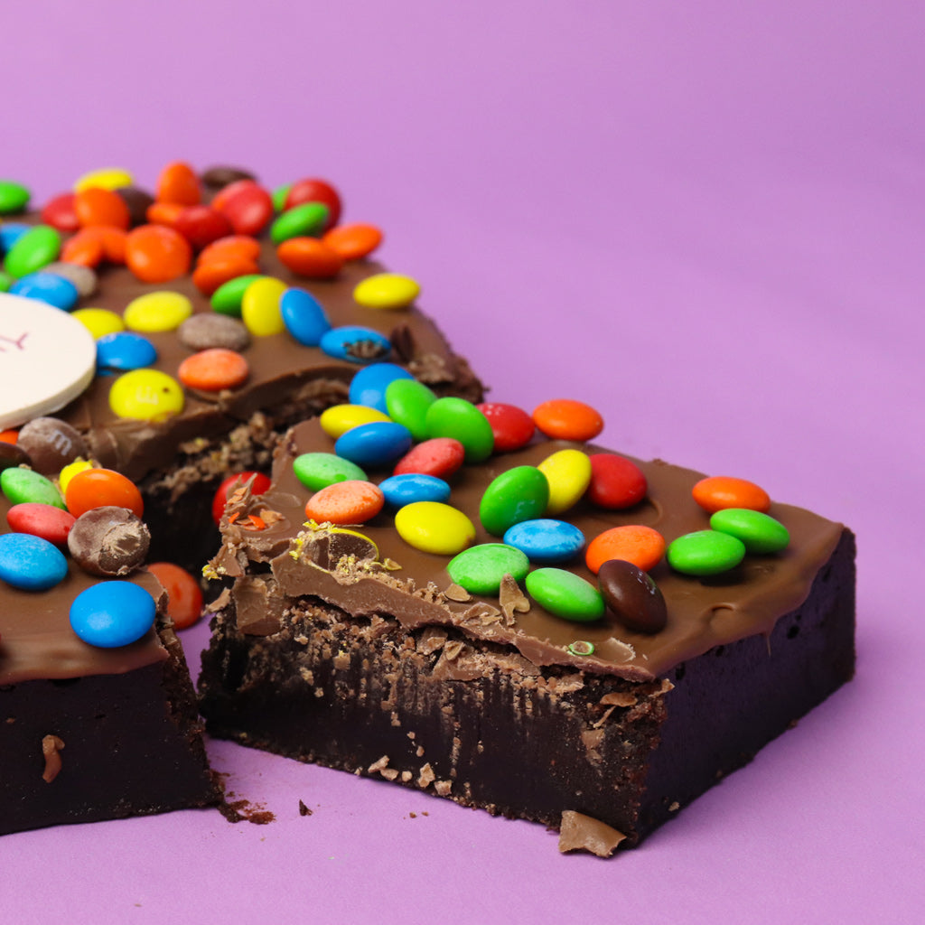 Chocolate brownie with colourful M&M pieces on a purple background