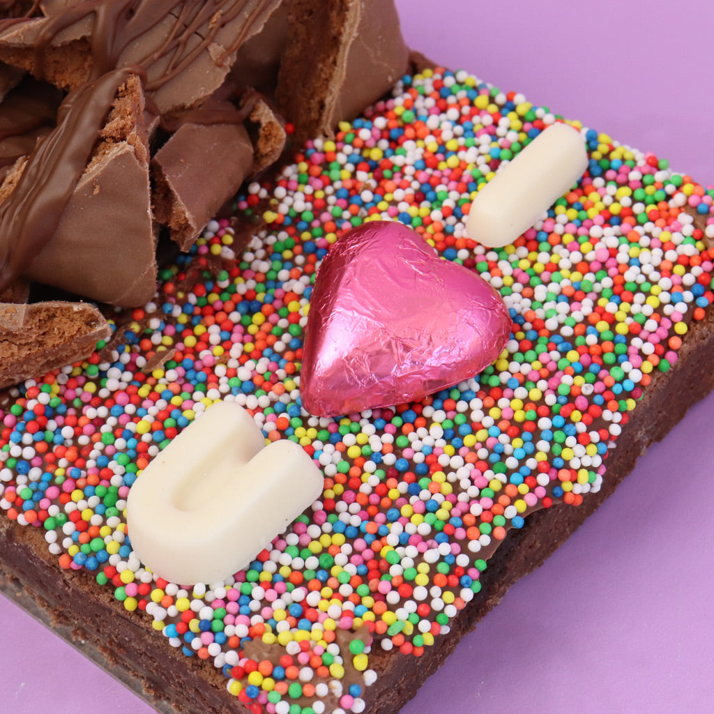 Chocolate bar with colorful sprinkles and a pink heart-shaped candy on a purple background
