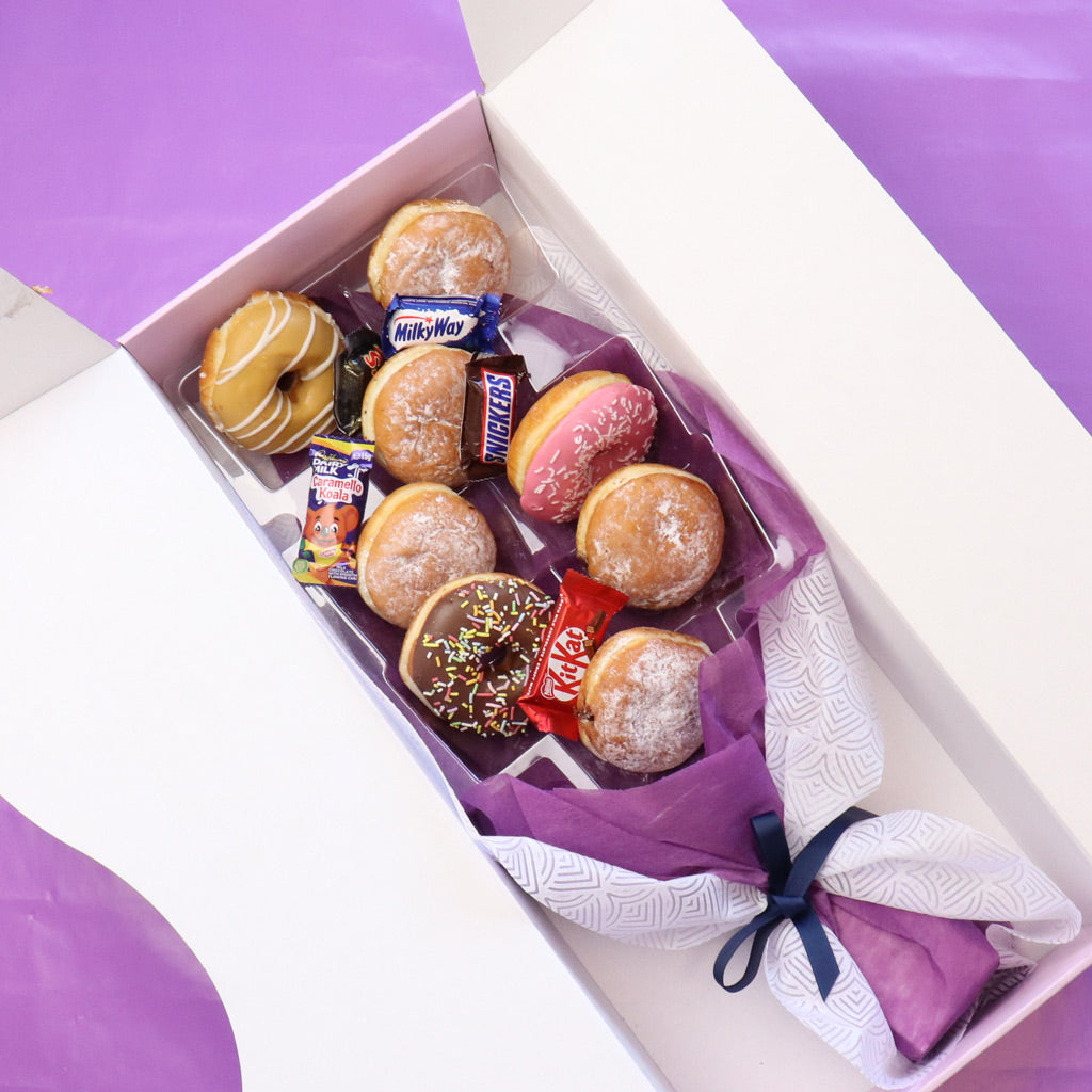 Box of assorted donuts and candy with a pink bow on a purple background