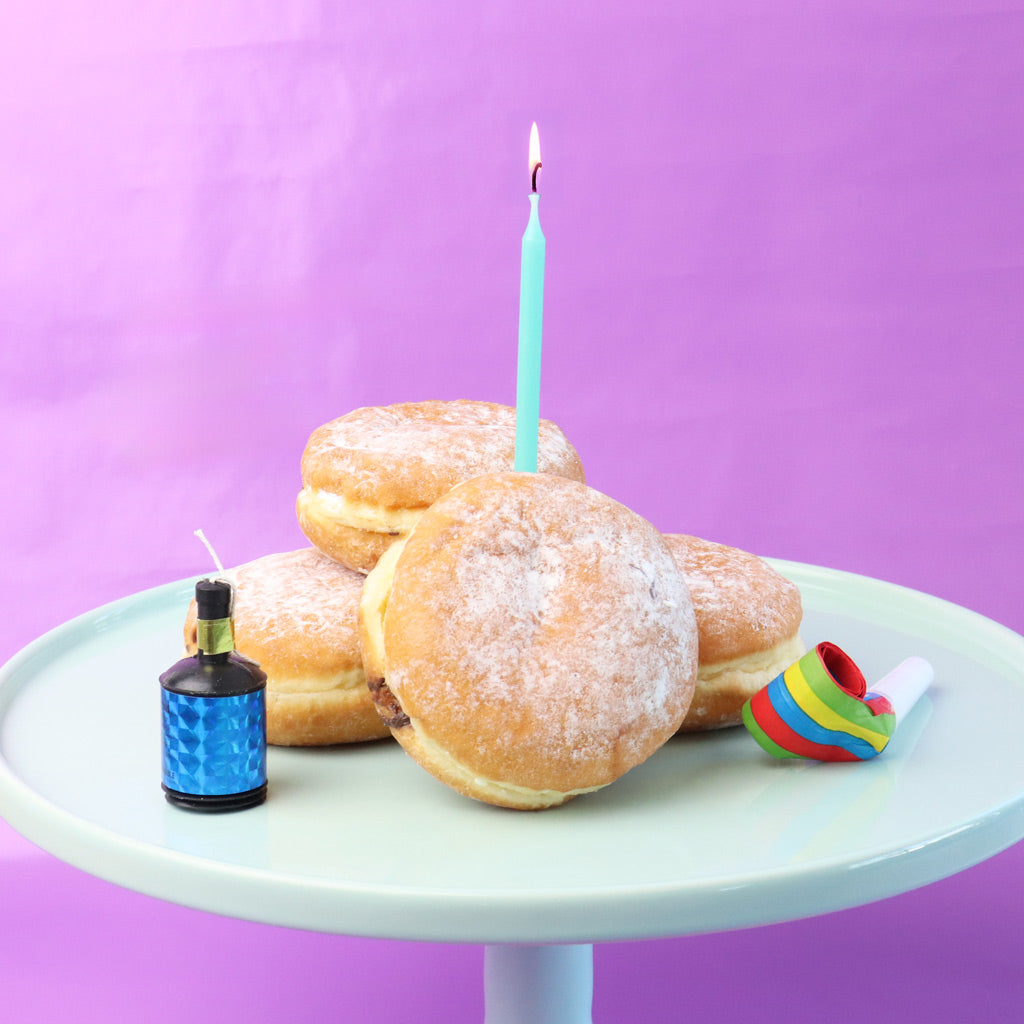 Donuts with a birthday candle on a white plate against a purple background