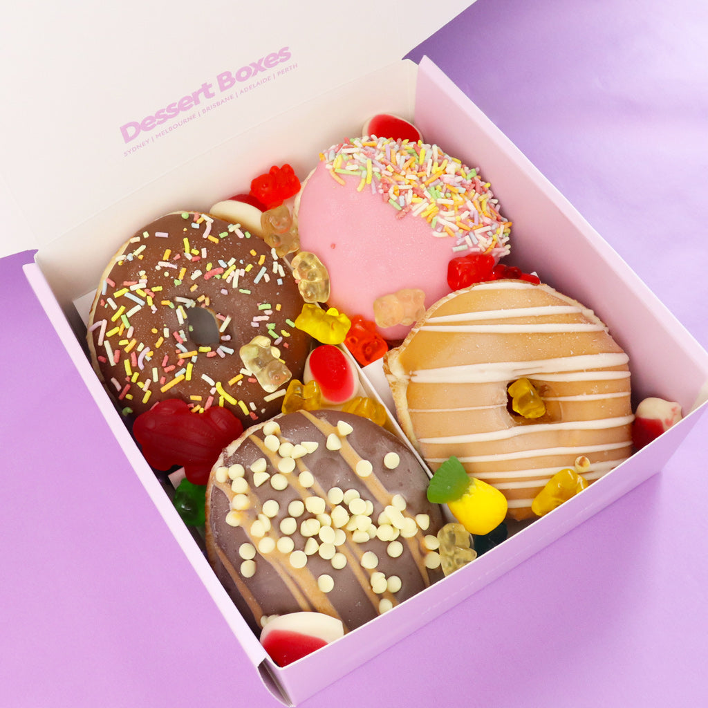 Assorted decorated donuts in a purple box by 'Dessert Boxes' 